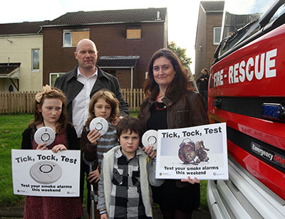 The Fitzsimmons family pictured next to fire appliance holding smoke alarms and 'Tick,Tock,Test' posters