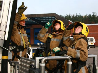 Two women in protective suits receive instruction from a firefighter whilst in standing in the cage of the Aerial Platform Ladder