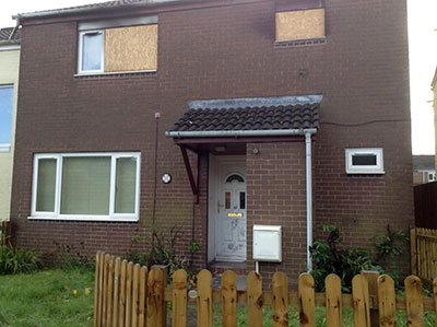 Photo of house from outside with upstairs windows boarded up and signs of fire damage on the brickwork and guttering