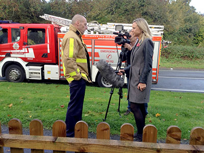 Firefighter and reporter pictured in front of a fire appliance with camera man filming
