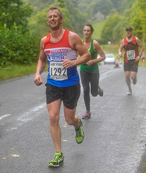 Steve pictured running along a road, wet through on a rainy day, with two runners behind him