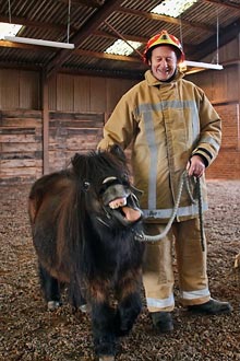Stuart West holding a Shetland pony which is pulling a face at the camera